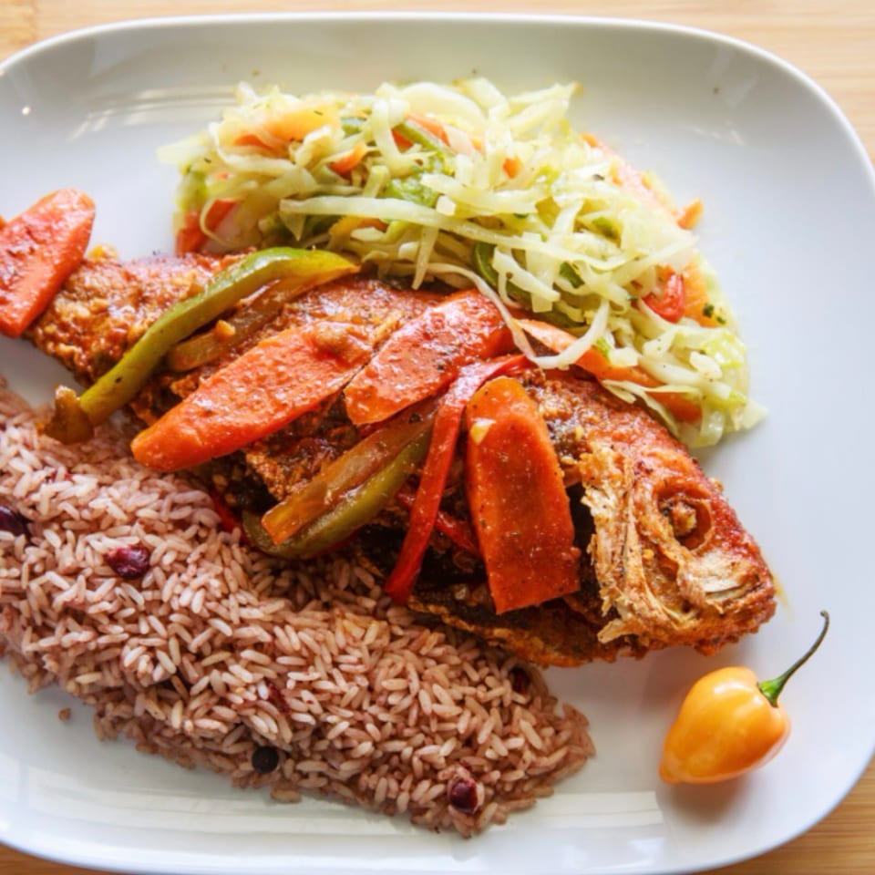 Fried whole fish with rice and peas, steamed cabbage, and a scotch bonnet pepper.