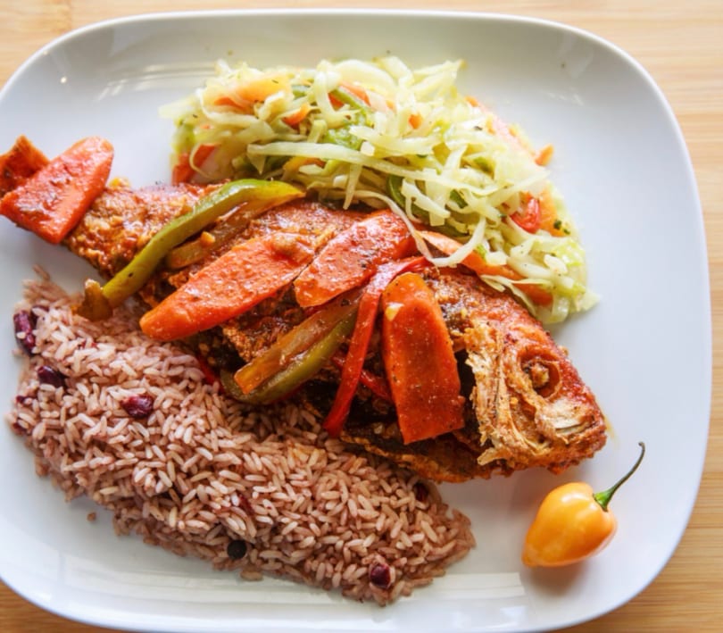 Fried whole fish with rice and peas, steamed cabbage, and a scotch bonnet pepper.