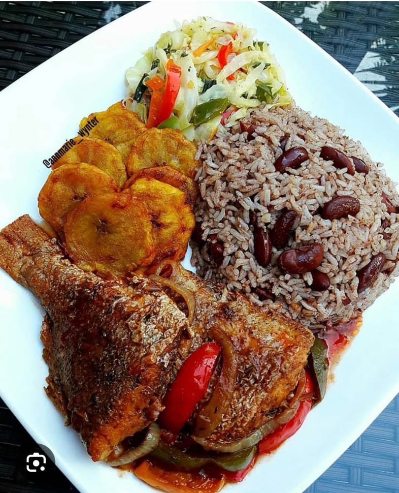 A plate of brown stew fish with rice and peas, fried plantains, and steamed cabbage.